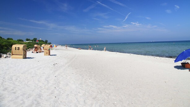 Une plage de sable blanc, un ciel bleu azur et quelques cabanes de plage.