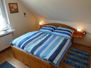 Une chambre à coucher avec un lit en bois, une literie à rayures, deux lampes de chevet, un petit tapis et une fenêtre avec des stores.