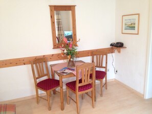 Un coin repas avec une table et quatre chaises, le tout encadré de bois, agrémenté d’un vase de fleurs, d’un miroir et d’un téléphone posé sur une étagère.