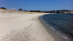 A sandy beach with gentle waves, a clear sky, and distant buildings. - FW4 - Rohrdachhus, Germany (Middelhagen)