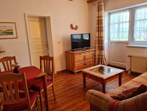 Un salon chaleureux avec un plancher en bois, un canapé, une table basse et un téléviseur posé sur un meuble en bois.