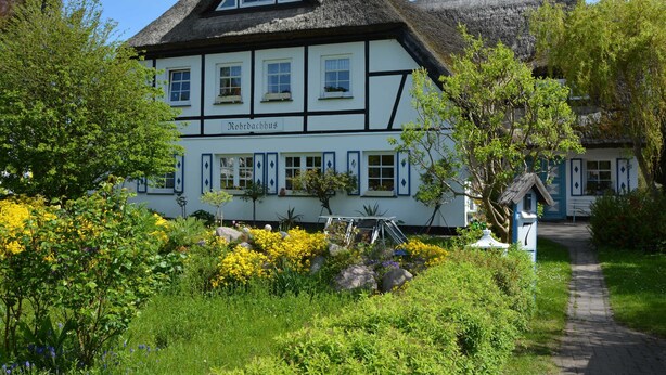 A traditional half-timbered building with a thatched roof, surrounded by lush greenery and flowering plants. - FW4 - Rohrdachhus, Germany (Middelhagen)