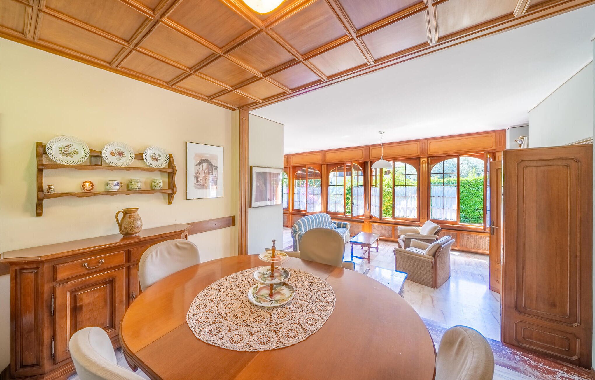 A dining area with a round table, chairs, wooden paneling, and large windows.