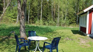A small outdoor seating area with a round table and four chairs, surrounded by a grassy lawn and a forested backdrop. - 3 bedroom stunning home in Häradsbäck (Häradsbäck)