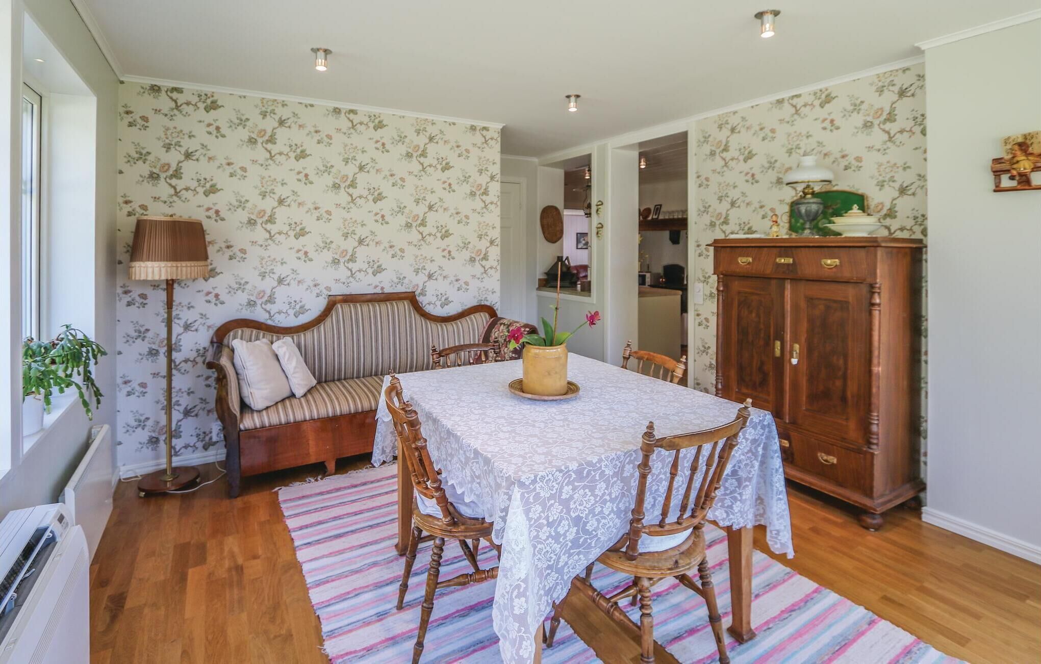 Un coin repas avec une table dressée pour quatre personnes, entourée de chaises en bois. On aperçoit également un canapé et un meuble.