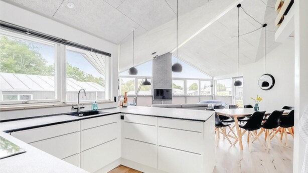 A modern kitchen with a large island, white cabinetry, and a dining area with black chairs. - Awesome home in Haderslev with sauna (Haderslev)