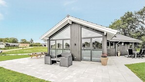 A modern building with large glass windows, a covered patio area with outdoor seating, and a small adjacent structure with a tiled roof. - Awesome home in Haderslev with sauna (Haderslev)