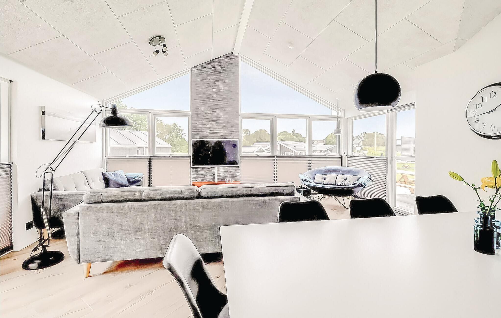 Una sala moderna con un sofá gris, una silla negra, una mesa de comedor y un ventanal con vistas al exterior.