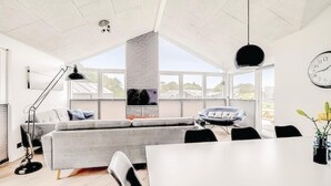 A modern living room with a grey sofa, a black chair, a dining table, and a large window offering a view of the outside. - Awesome home in Haderslev with sauna (Haderslev)