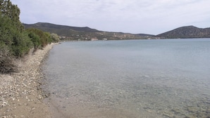 On aperçoit clairement une plage de galets, un lac paisible et des collines au loin.