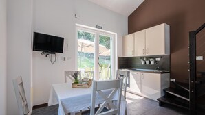 A compact kitchen with a dining area, a TV mounted on the wall, and a view of the outdoors through a glass door.