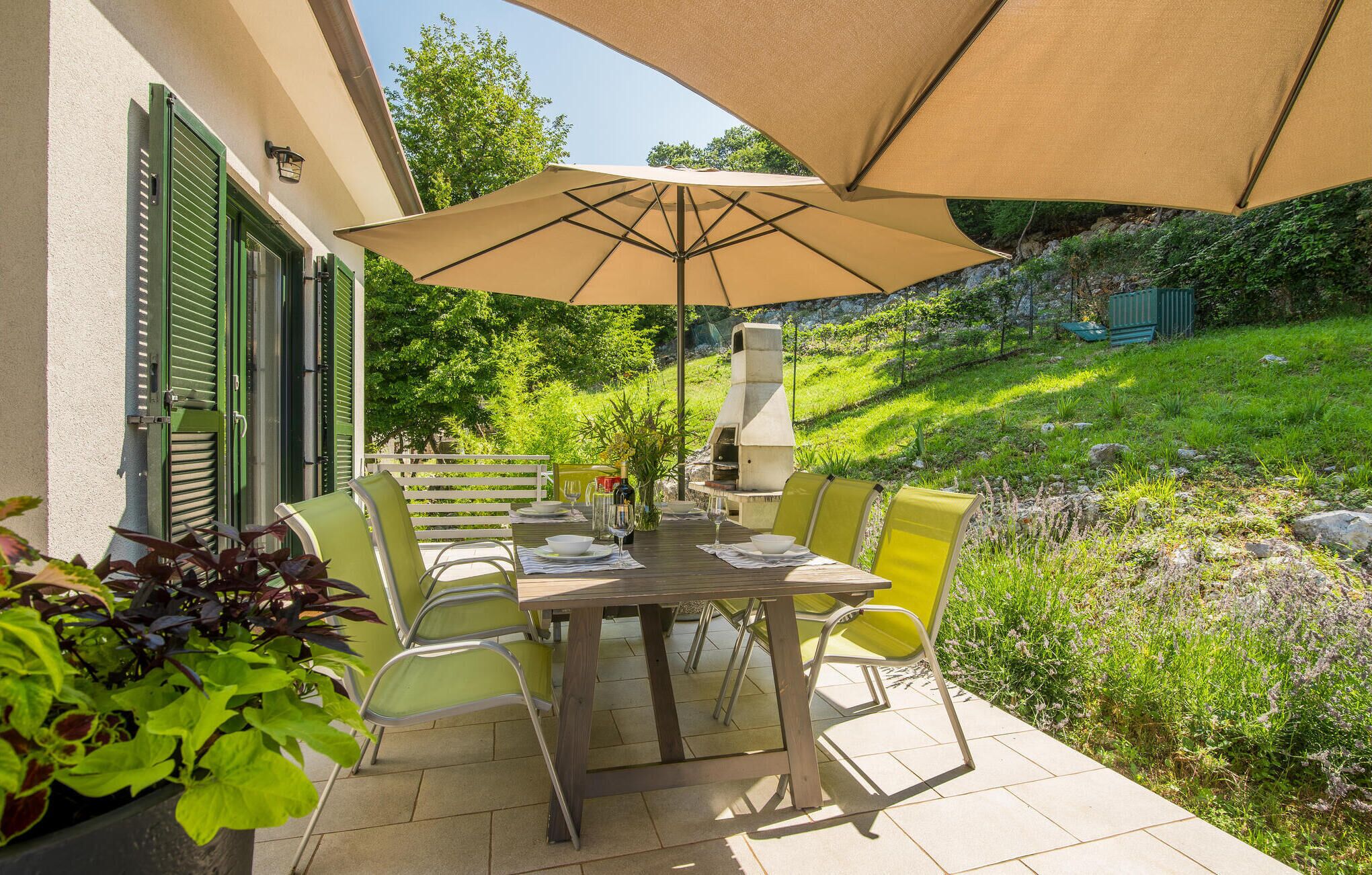 An outdoor patio with a table set for dining, surrounded by chairs, and a large umbrella providing shade.