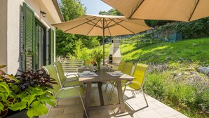 An outdoor patio with a table set for dining, surrounded by chairs, and a large umbrella providing shade.