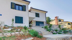 A two-story house with a stone facade, a stone staircase leading to the entrance, and a well-maintained garden with various plants and rocks.