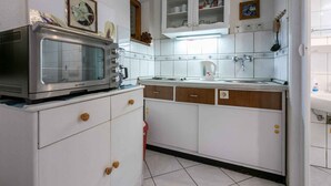 Une cuisine avec des meubles blancs, un four à micro-ondes, un évier et une horloge au mur.