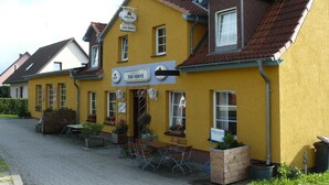 A yellow building with a sign reading "Zur Kurve" and outdoor seating. - Triple room (17) - Pension Zur Kurve (Prohn)