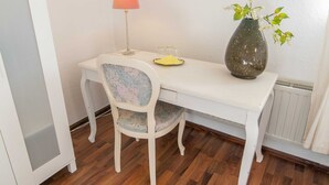 A white dining table with a floral-patterned chair, a vase with flowers, and a lamp on the table. - Triple room (17) - Pension Zur Kurve (Prohn)