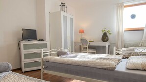 A bedroom with two beds, a desk, a chair, a wardrobe, and a television. - Triple room (17) - Pension Zur Kurve (Prohn)