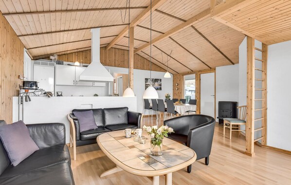 A spacious living area with a wooden ceiling, a black leather sofa, a coffee table, and a dining table with chairs.