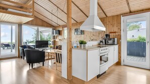 Uma cozinha moderna com ilha central, vigas de madeira no teto e uma porta de vidro deslizante que dá para uma área externa.