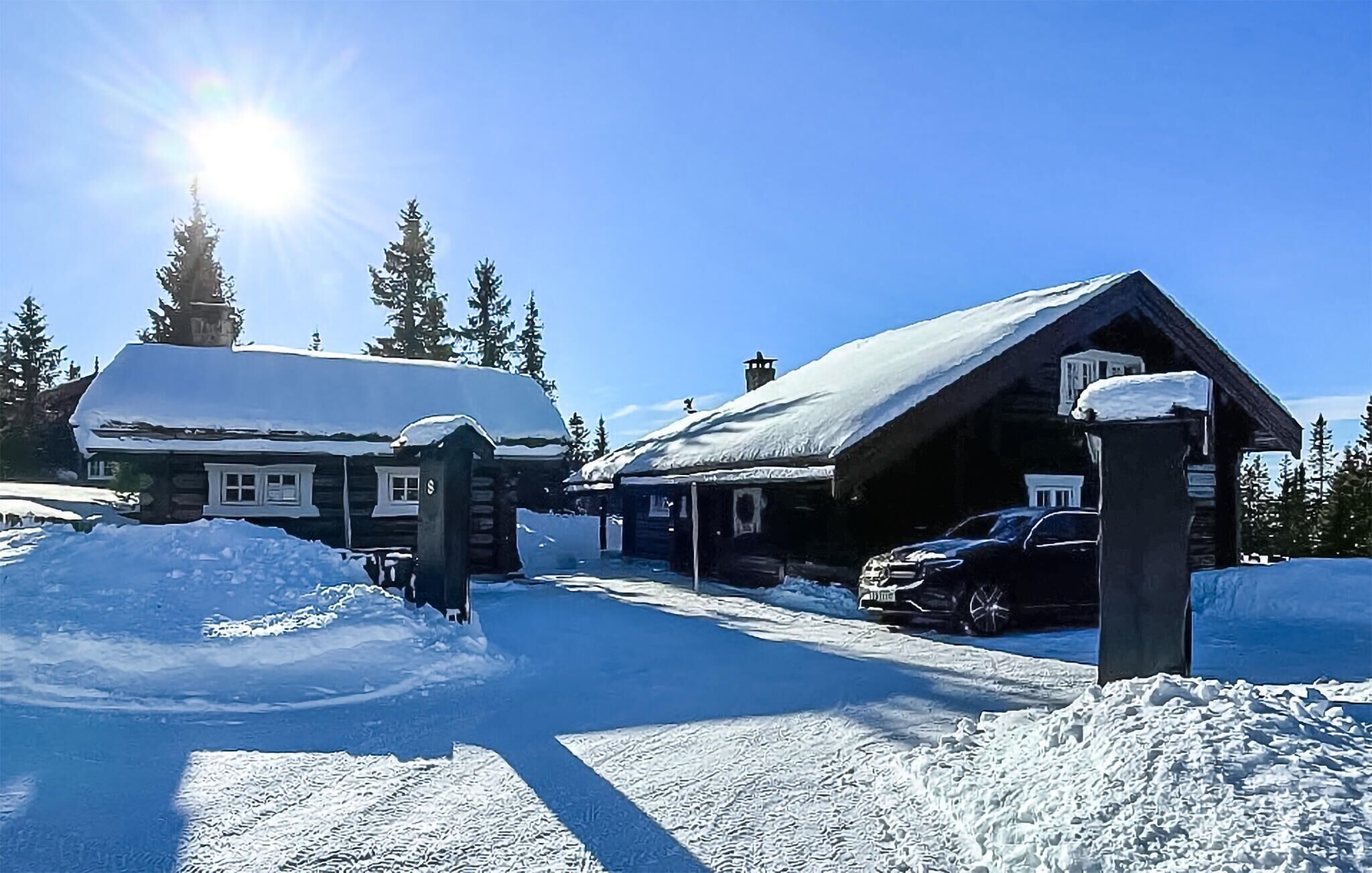 A snow-covered lodge with a wooden exterior, a covered driveway, and a car parked in front.