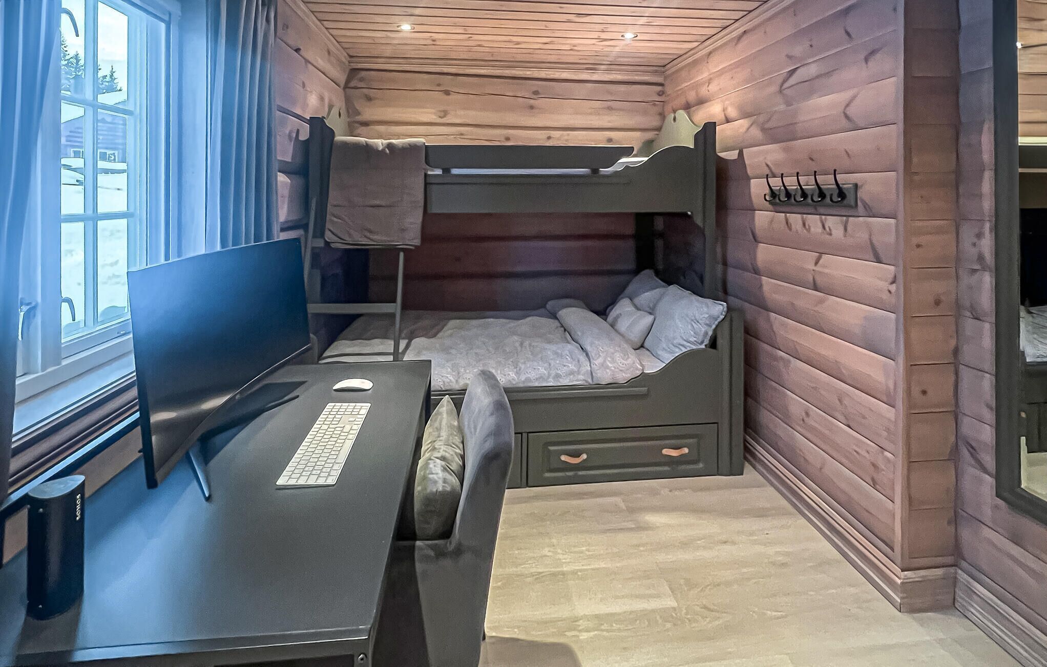 Une petite pièce avec un lit superposé, un bureau avec un ordinateur et une fenêtre.