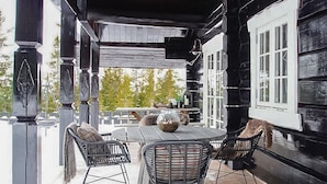 An outdoor patio with a round table and four chairs, surrounded by black wooden walls and white windows.