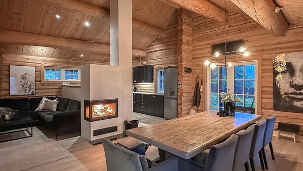 A log cabin interior with a dining area, kitchen, and living space.