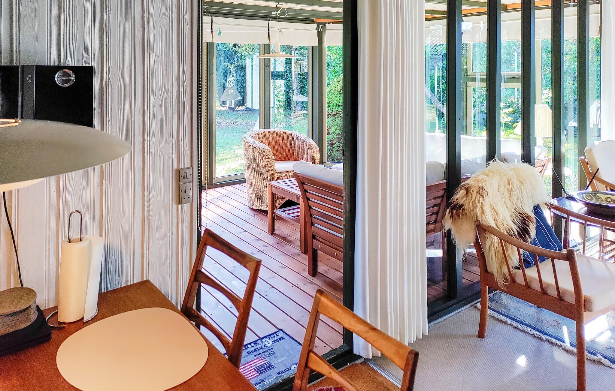 Ein Zimmer mit Holztisch, Stühlen, einer Rattan-Couch und Blick ins Freie durch große Fenster.