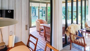 Une pièce avec une table en bois, des chaises, un canapé en osier et une vue sur l’extérieur grâce à de grandes fenêtres.