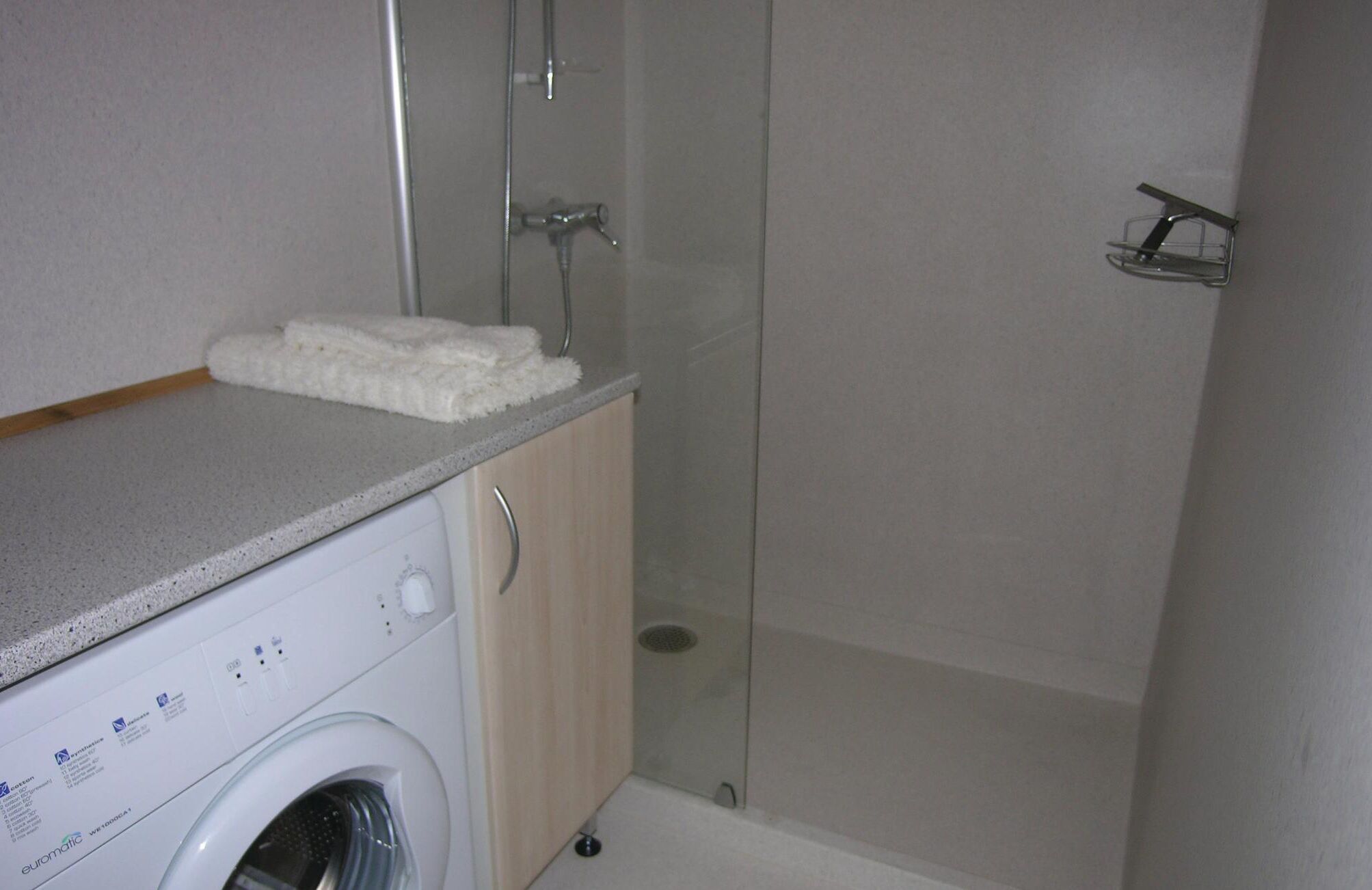 A compact bathroom with a washing machine, a glass shower enclosure, and a towel rack.