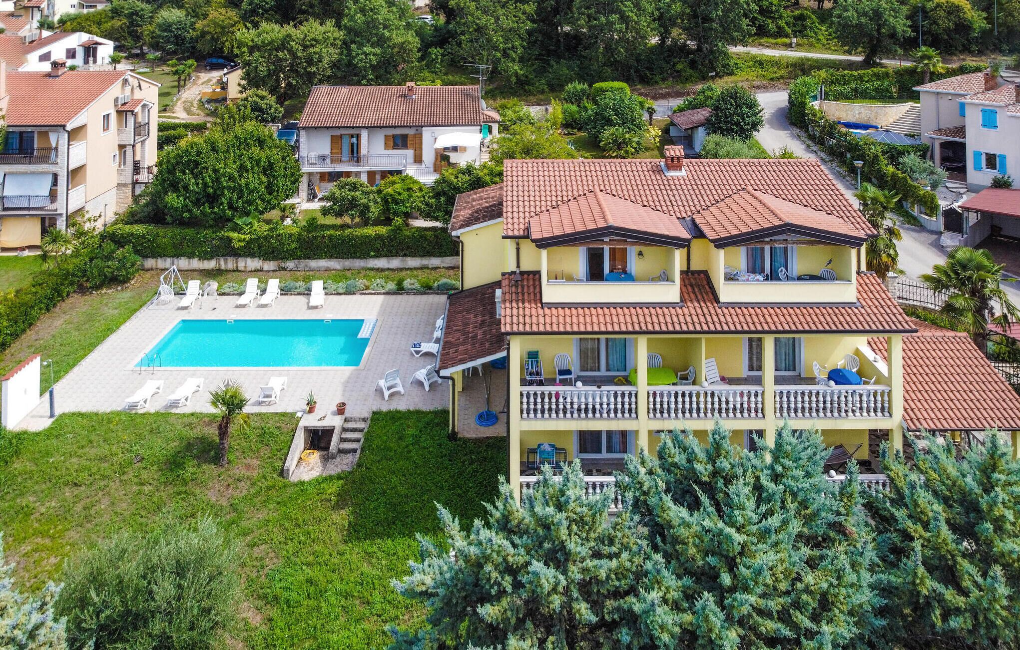 A two-story house with a swimming pool, surrounded by greenery and other residential buildings.