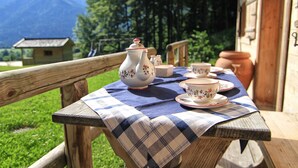 Un tavolo di legno con tovaglia a quadri, apparecchiato con tazze da tè e teiera, con vista su un paesaggio montano.