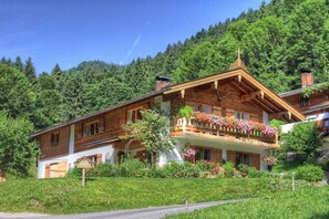 Eine Holzhütte mit Balkon, umgeben von üppiger Vegetation und einem bewaldeten Hang.