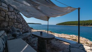 A stone wall, a table with a blue cup, and a view of the sea and a green island.
