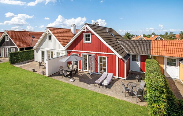 Una casa de color rojo y blanco con un patio, una zona de estar al aire libre cubierta y un césped bien cuidado.