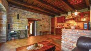 A rustic interior with stone walls, wooden beams, a stone fireplace, and a kitchen area with wooden cabinets.