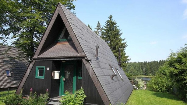 Ein dreieckiges Holzgebäude mit geneigtem Dach, einer grünen Tür und einer kleinen Veranda.