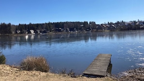 Ein ruhiger See mit einem hölzernen Steg, der ins Wasser führt, umgeben von Häusern und Bäumen.