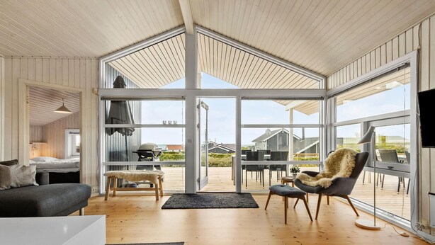 A spacious living room with a large glass door leading to an outdoor deck, wooden flooring, and a cozy seating area with a fur throw chair. - Beautiful home in Rønde with sauna (Rønde)