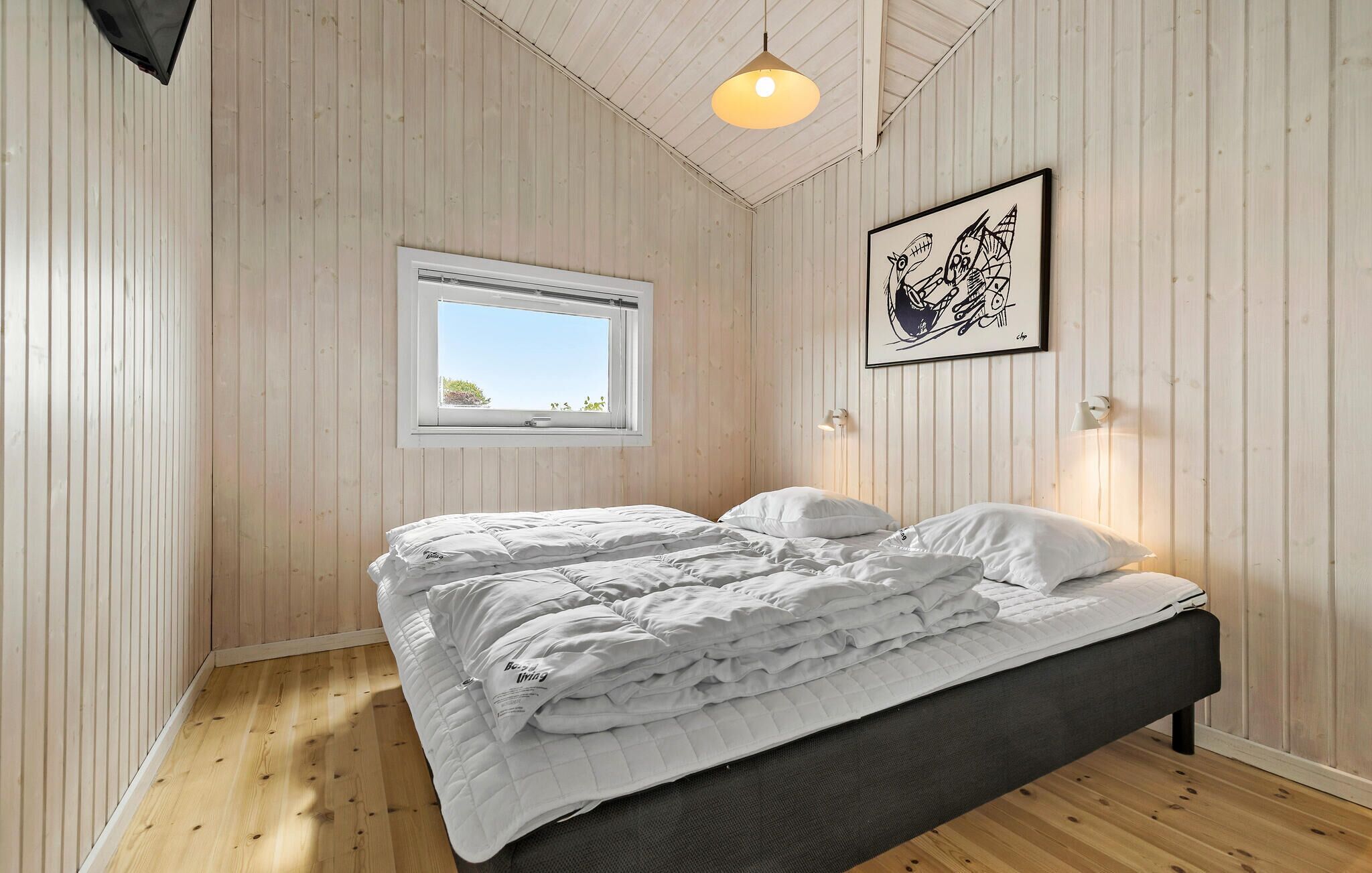 A bedroom with a bed, a window, and a wall-mounted light fixture.