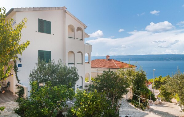 A coastal building with a white facade, green shutters, and a red-tiled roof. It features a balcony with a stone staircase leading up to it. - Beach front apartment in Stanici (Stanici)