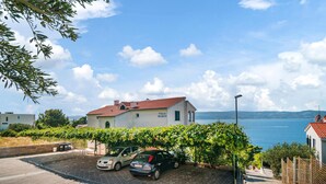 Een villa met een rode dakbedekking, geparkeerde auto's en uitzicht op zee.