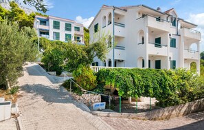 A multi-story building with balconies, a paved pathway leading to the entrance, and greenery around the property. - Beach front apartment in Stanici (Stanici)