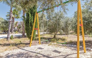 Relax in a serene outdoor space surrounded by olive and palm trees, featuring a charming swing set amidst a lush landscape.