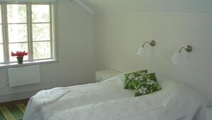 A bedroom with a bed, a nightstand, a window with flowers, and wall-mounted lamps. - Cozy home in Katrineholm with lake view (Katrineholm)