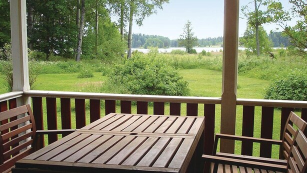 A wooden deck with a table and chairs, overlooking a grassy area with trees and a body of water. - Cozy home in Katrineholm with lake view (Katrineholm)