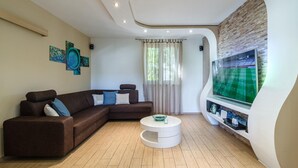 A modern living room with a brown sectional sofa, a white coffee table, and a large flat-screen TV mounted on a brick wall. - Amazing home in Milna (Milna)