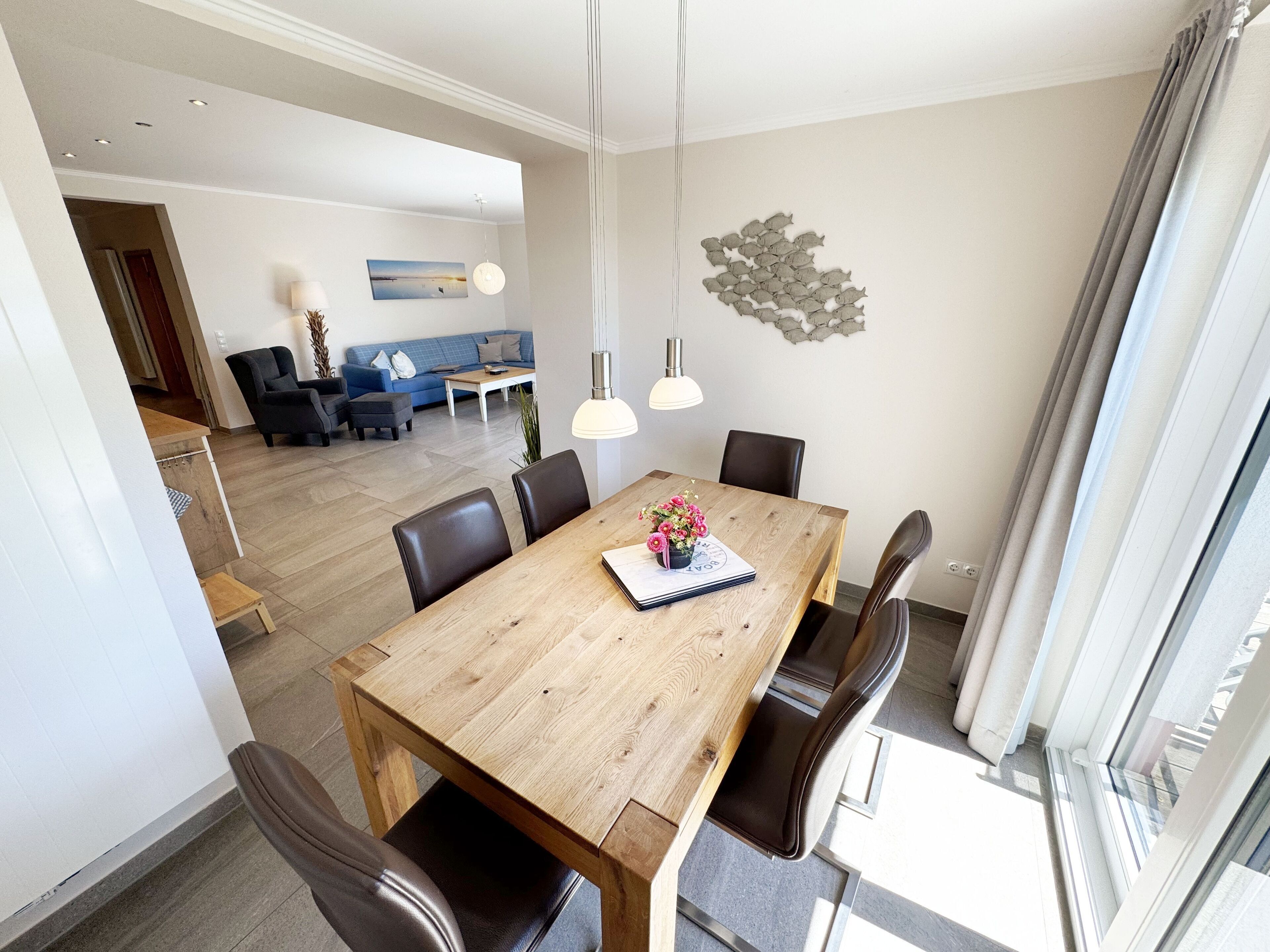 Un espace de salle à manger moderne avec une table en bois, des chaises noires et des luminaires suspendus.