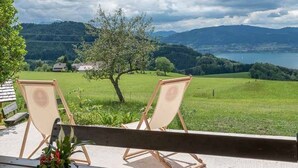 Dos sillones de madera en un balcón con vista a un paisaje verde con un árbol y colinas distantes.